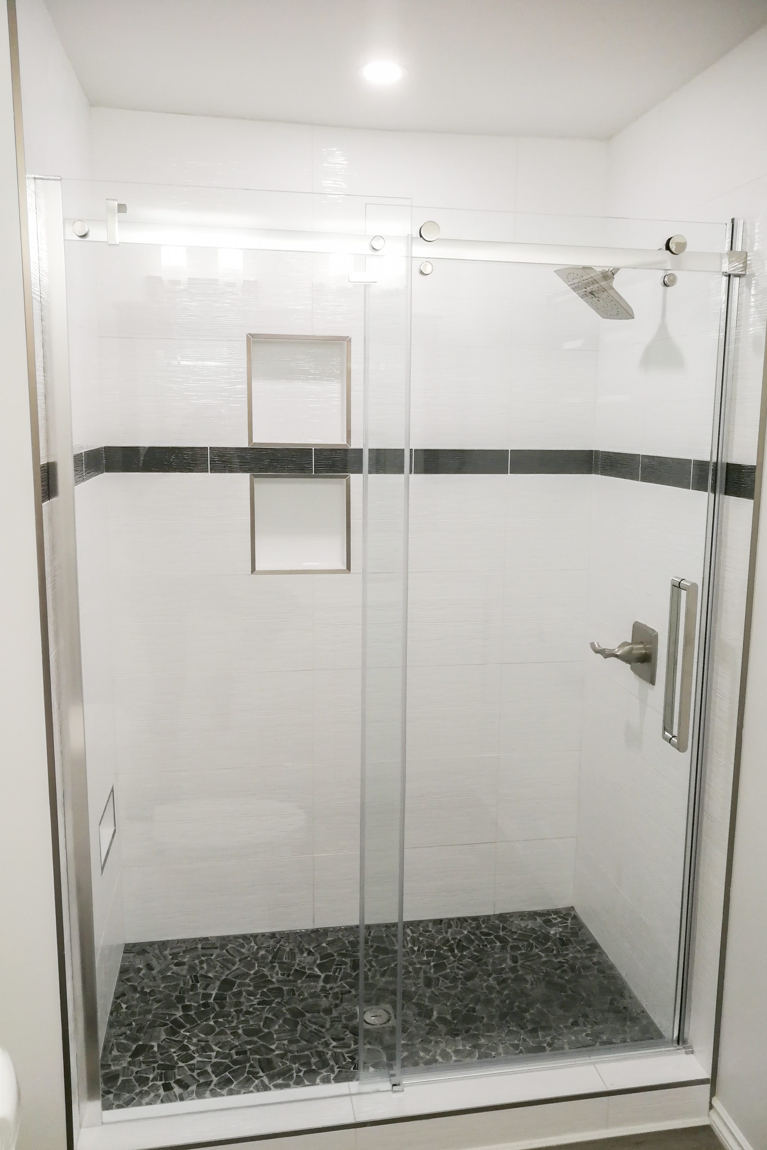 A newly-renovated shower area with stone flooring and modern showerheads for a bathroom renovation project