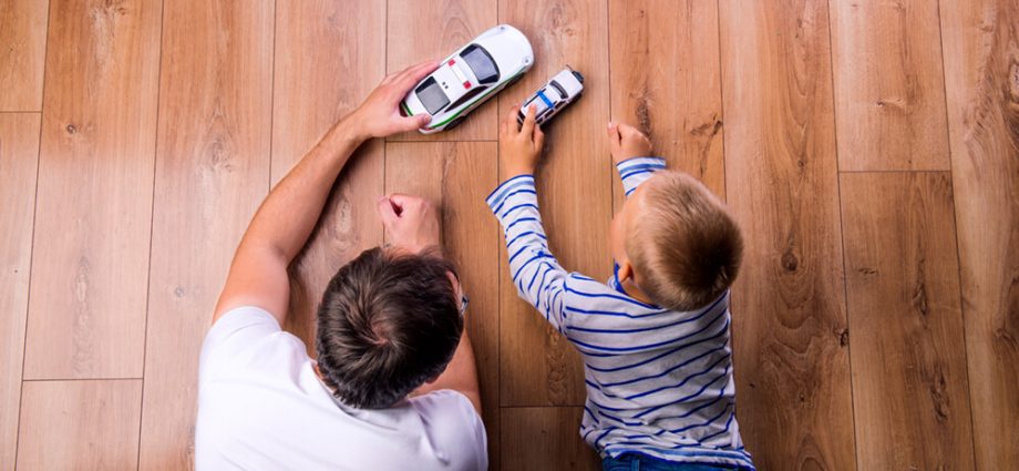 Dad and son playing cars on wood flooring